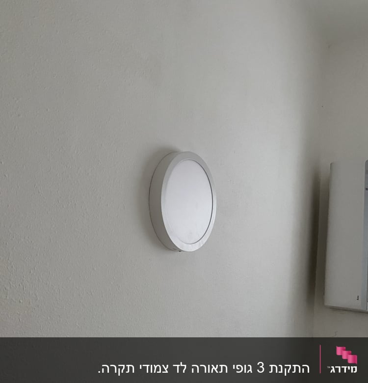 מנורה עגולה על קיר לבן ליד ארון חשמל